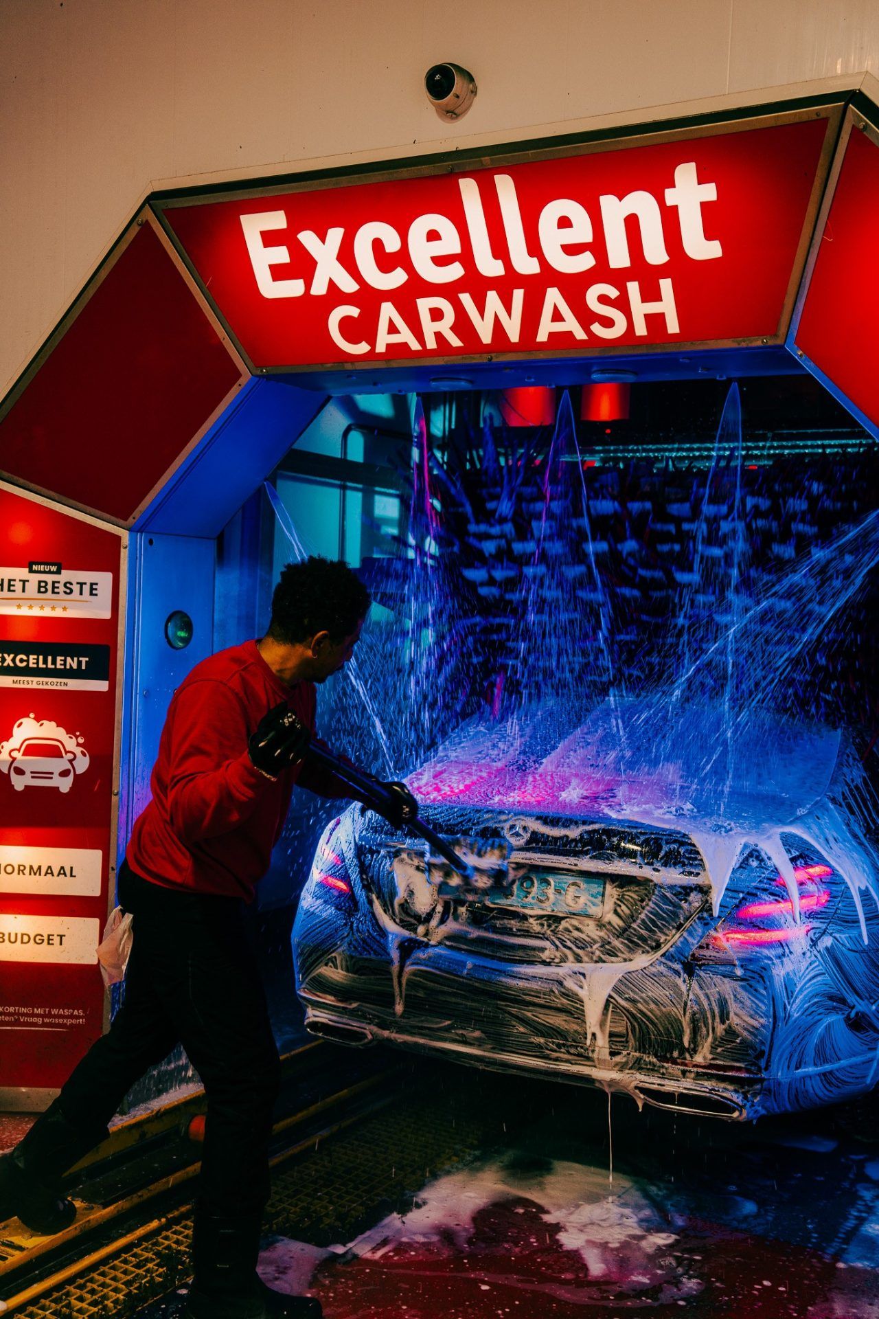 Medewerker van Excellent Carwash spuit schuim op de voorzijde van een auto bij de handmatige voorwas.